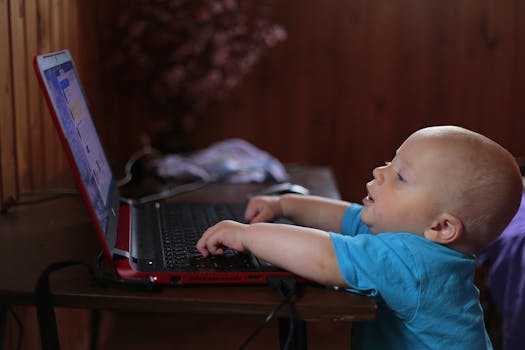 Cute baby boy engaged with a laptop indoors, showing early tech curiosity.