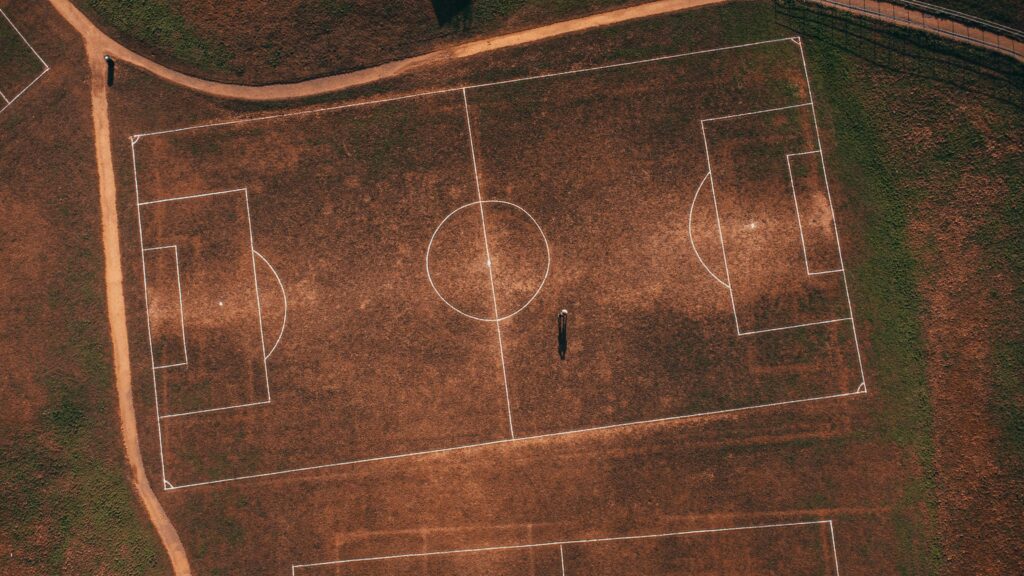 pexels-photo-11300376-11300376 Aerial view of an empty rustic soccer field with a solitary person, showcasing detailed grass lines.