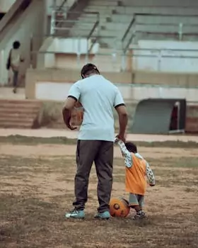 A father and child bonding over a soccer ball on an outdoor field.
