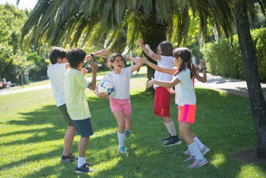 pexels-photo-8813501-8813501 Group of happy children playing football under a palm tree in a sunny park.