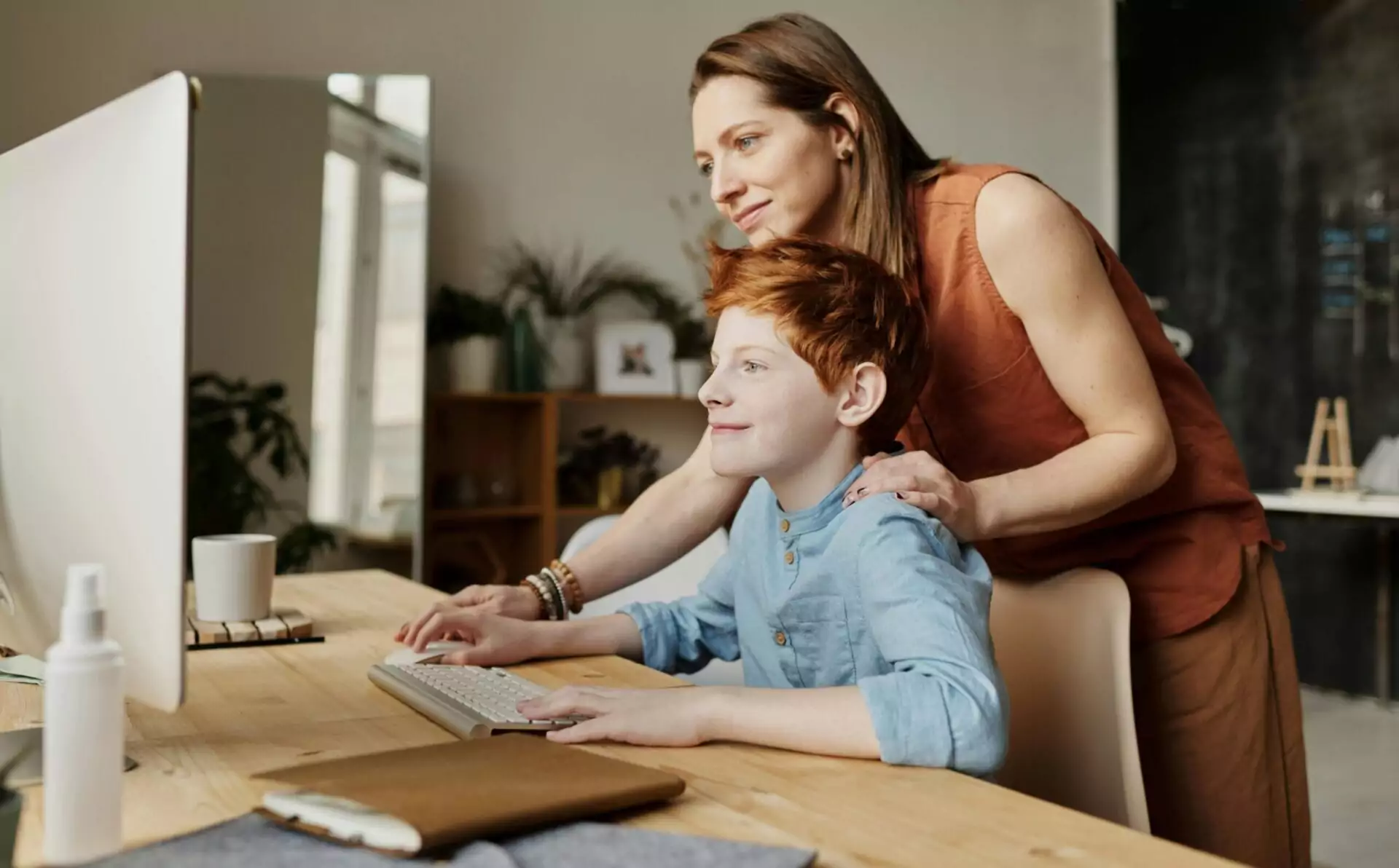 A mother and her child smiling while using a computer at home, focused on learning.